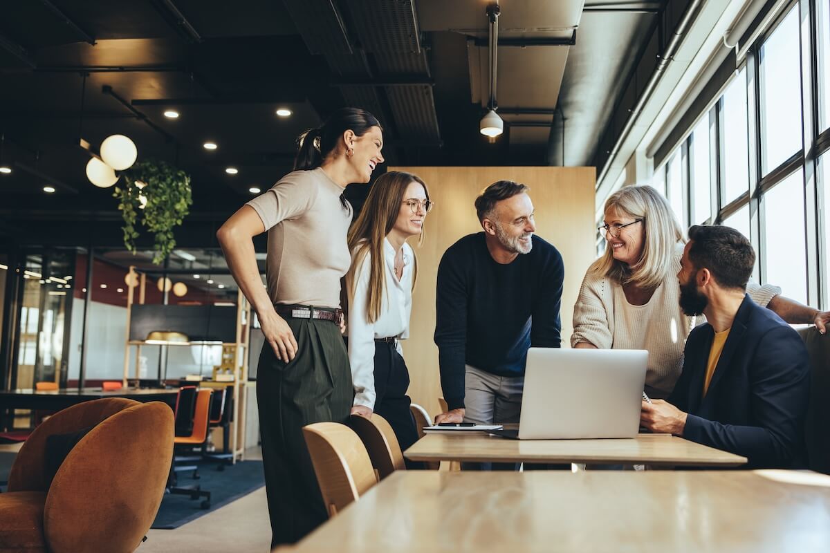 Smiling colleagues talking around a laptop in an office