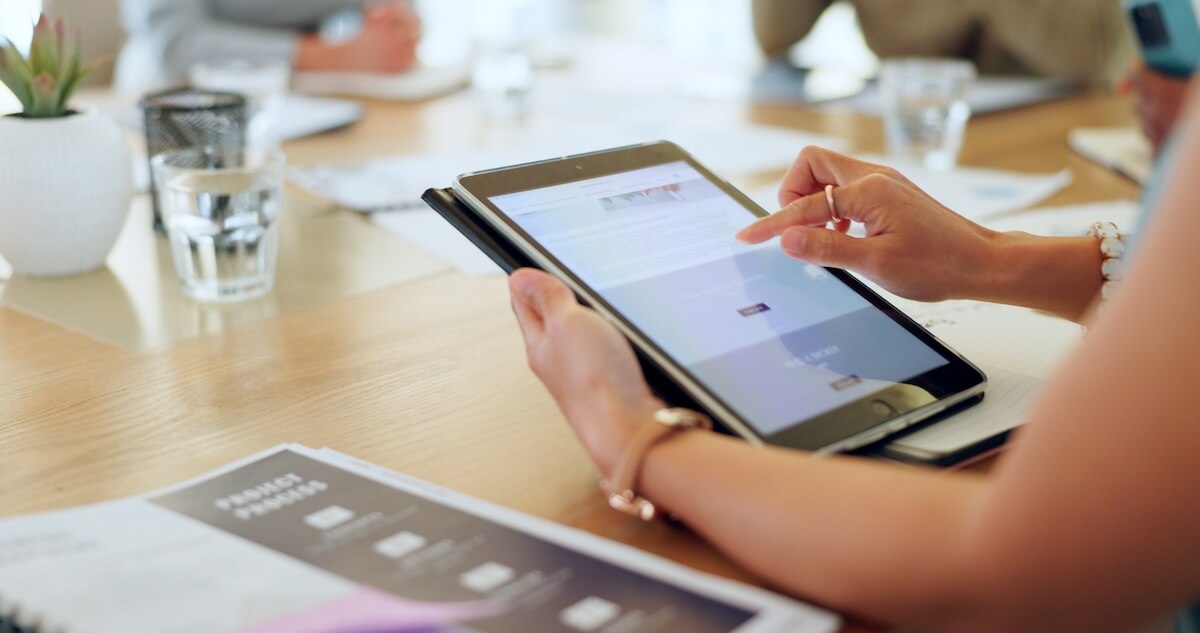Hands scrolling through a newsletter on a tablet at a meeting table