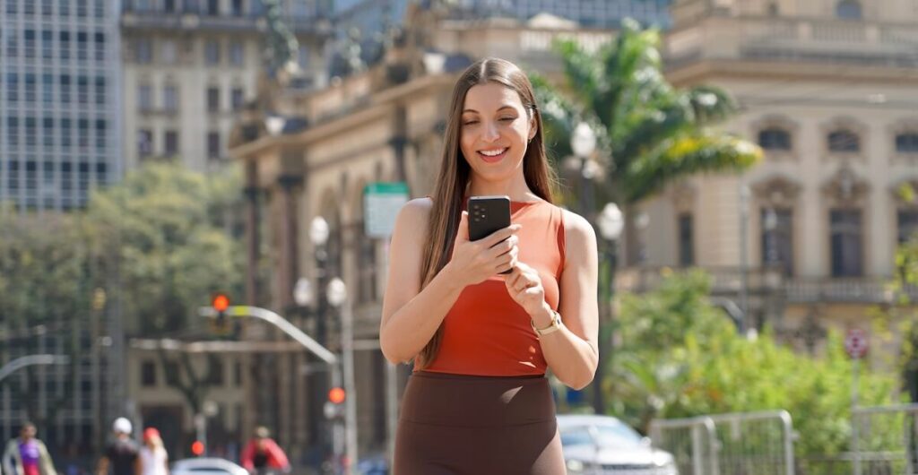 Smiling woman using her smartphone on a sunny city street